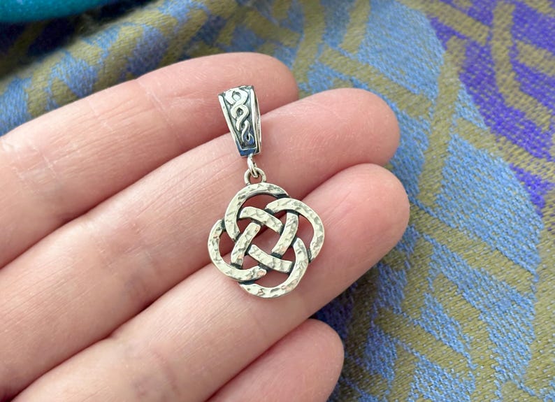 May include: A silver Celtic knot pendant with a textured finish. The pendant is in the shape of a four-leaf clover and has a loop at the top for attaching to a chain.