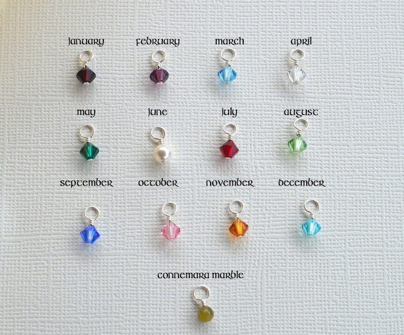 May include: Twelve crystal charms in various colors, each representing a different month of the year. The charms are displayed on a white surface with the month names written above each charm. The charms are small and delicate, and they would make a beautiful addition to any jewelry piece.