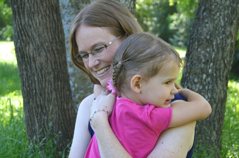 Puede incluir: Una mujer con cabello casta&ntilde;o y gafas sostiene a una ni&ntilde;a peque&ntilde;a con cabello casta&ntilde;o. La mujer lleva una camisa azul y la ni&ntilde;a lleva una camisa rosa. La ni&ntilde;a sonr&iacute;e y mira a la c&aacute;mara.