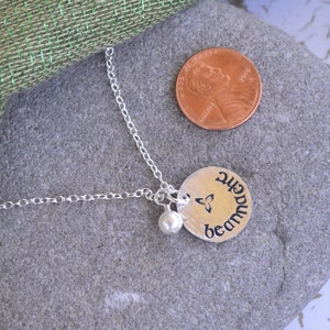 K&ouml;nnte beinhalten: Silberne Halskette mit einem runden Anh&auml;nger, der einen keltischen Knoten und das Wort "Sch&ouml;nheit" in g&auml;lischer Schrift zeigt. Der Anh&auml;nger ist an einer silbernen Kette mit einer kleinen Perle befestigt.