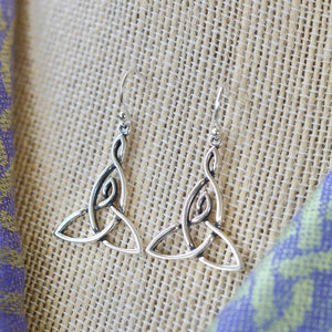 May include: A pair of silver Celtic knot earrings with a triangular shape. The earrings are hanging from a simple hook.