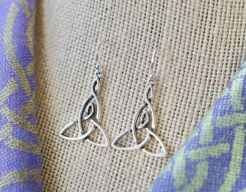 May include: A pair of silver Celtic knot earrings with a triangular shape. The earrings are hanging from a simple hook.
