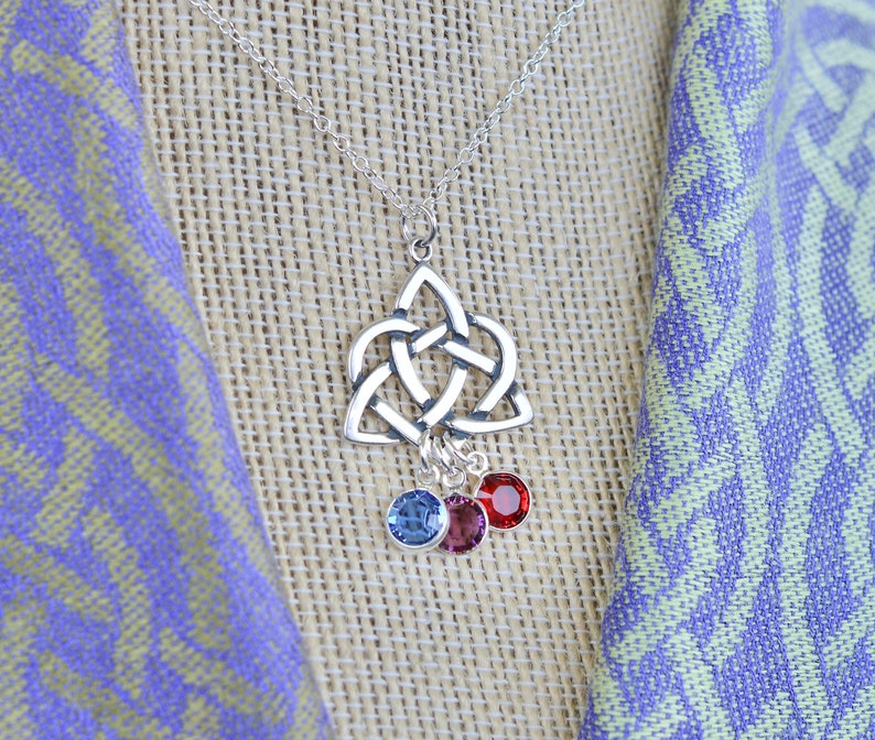 Puede incluir: Un collar con un colgante de nudo celta plateado y tres cristales colgantes: azul, rosa y rojo.