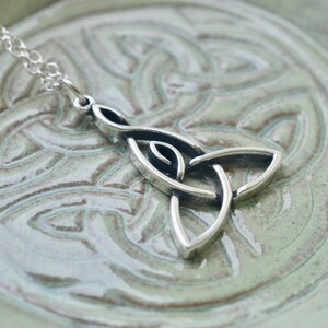May include: Silver Celtic knot pendant necklace with a trinity knot design. The pendant is on a light green background.