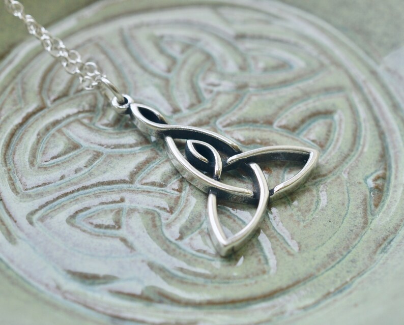 May include: Silver Celtic knot pendant necklace with a trinity knot design. The pendant is on a light green background.