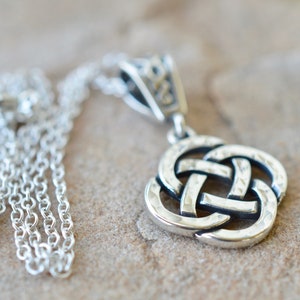 May include: A silver Celtic knot pendant necklace with a detailed, textured design. The chain is a delicate silver chain.