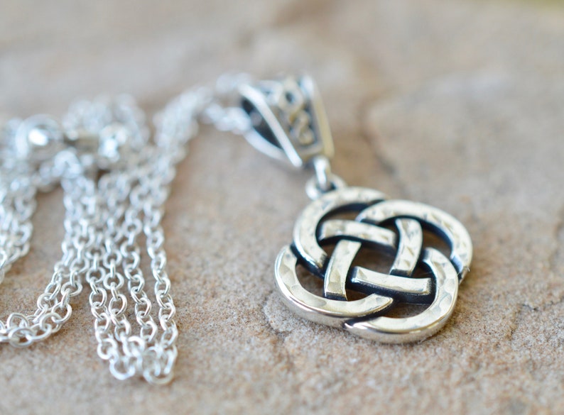 May include: A silver Celtic knot pendant necklace with a detailed, textured design. The chain is a delicate silver chain.