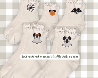 Puede incluir: Un conjunto de cinco calcetines tobilleros de color blanco roto con puños de volantes, cada uno con un icono bordado diferente de temática de Halloween, incluyendo una telaraña, una calabaza, un murciélago y dos fantasmas. Se lee el texto Embroidered Women's Ruffle Ankle Socks.