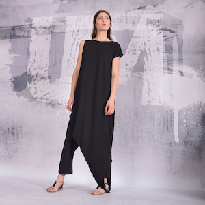 Puede incluir: Un vestido negro asim&eacute;trico con manga corta y cuello alto. El vestido est&aacute; hecho de una tela suave y fluida y tiene un corte holgado.