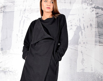 May include: A black long-sleeved jacket with a draped collar and pockets. The jacket is worn over white pants and black ankle boots.