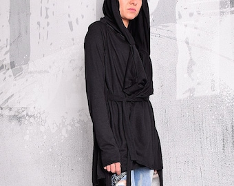 May include: A black hooded cardigan with a long, flowing design and a tie belt. The cardigan is worn over a pair of blue jeans with distressed details.