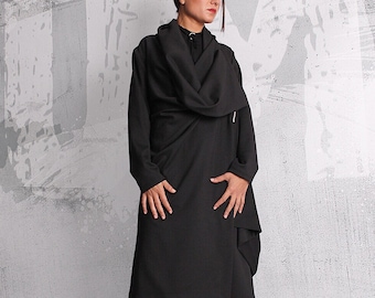 May include: A black dress with a long, flowing skirt and a high neckline. The dress has a unique design with a wrap-around style and a zipper detail. The model is wearing black ankle boots.