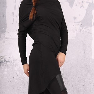 May include: A black long-sleeved tunic with a draped neckline and a high-low hemline. The tunic is paired with black leggings that have a leather panel and mesh detailing.