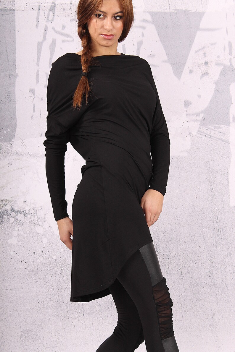 May include: A black long-sleeved tunic with a draped neckline and a high-low hemline. The tunic is paired with black leggings that have a leather panel and mesh detailing.