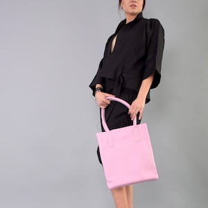 May include: A woman wearing a black top and skirt holds a pink leather tote bag.