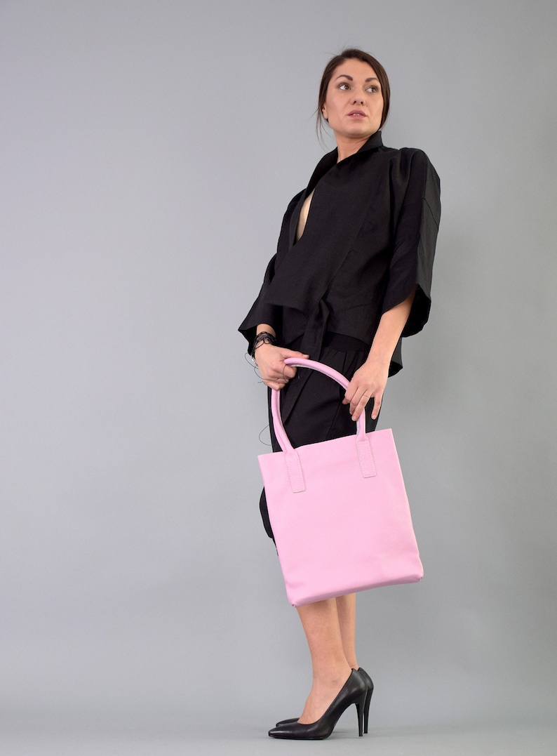 May include: A woman wearing a black top and skirt holds a pink leather tote bag.
