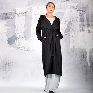 May include: A long black hooded cardigan with a tie belt. The cardigan is worn over a grey top and grey pants.