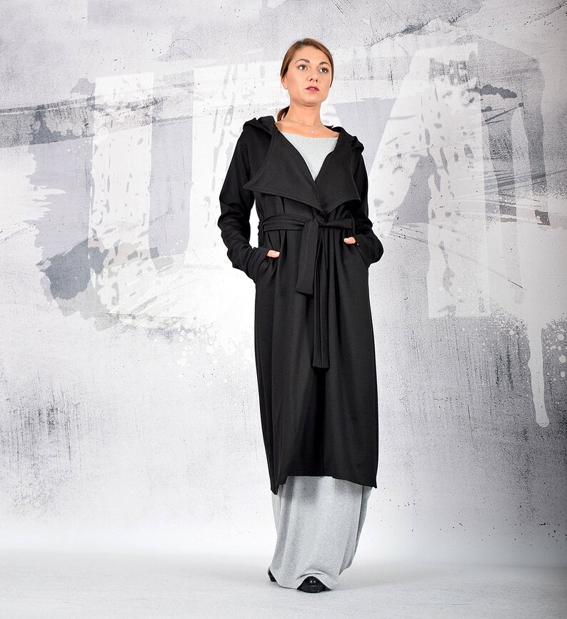 May include: A long black hooded cardigan with a tie belt. The cardigan is worn over a grey top and grey pants.