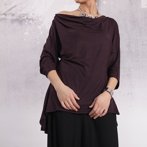 Puede incluir: Una blusa de manga larga, de color morado oscuro, con cuello de pico y un dobladillo ligeramente asim&eacute;trico. La blusa est&aacute; hecha de una tela suave y fluida.