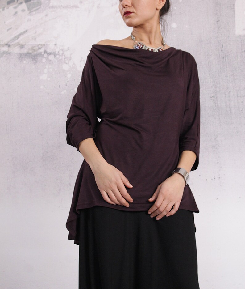 Puede incluir: Una blusa de manga larga, de color morado oscuro, con cuello de pico y un dobladillo ligeramente asim&eacute;trico. La blusa est&aacute; hecha de una tela suave y fluida.