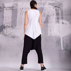 Op de afbeelding: Een wit tanktop met een uniek ontwerp op de rug, gecombineerd met een zwarte broek. Het topje heeft een gerimpelde zoom en een contrasterend zwart detail op de rug.