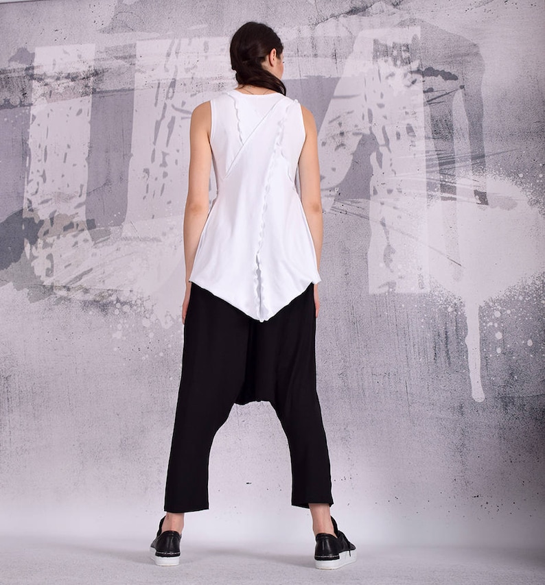 Op de afbeelding: Een wit tanktop met een uniek ontwerp op de rug, gecombineerd met een zwarte broek. Het topje heeft een gerimpelde zoom en een contrasterend zwart detail op de rug.