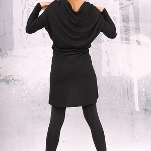 May include: A black long-sleeved tunic dress with a cowl neck and a loose fit. The dress is paired with black leggings and black fur-trimmed boots.