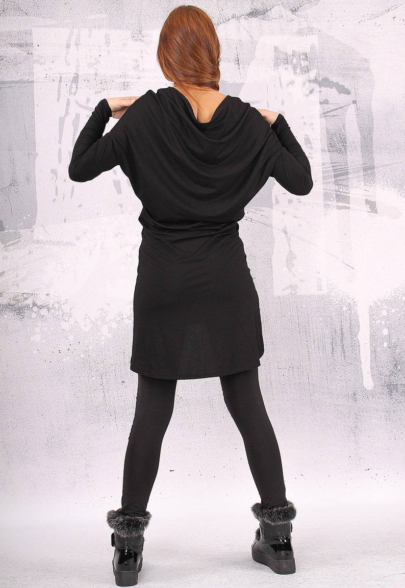 May include: A black long-sleeved tunic dress with a cowl neck and a loose fit. The dress is paired with black leggings and black fur-trimmed boots.