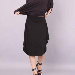 May include: A black midi skirt with a flowing, asymmetrical hemline. The skirt is made of a soft, stretchy fabric and falls just below the knee.
