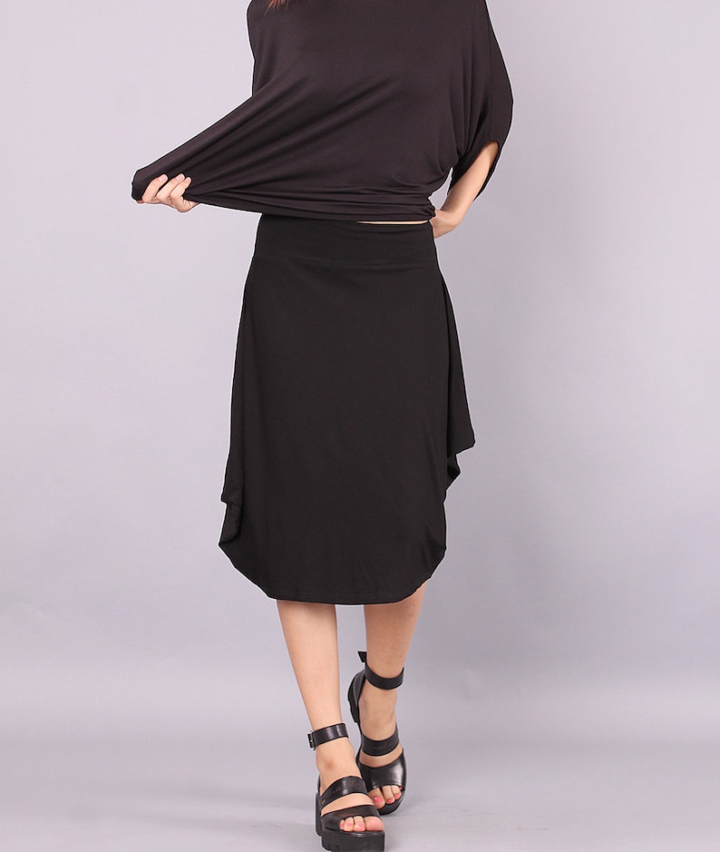 May include: A black midi skirt with a flowing, asymmetrical hemline. The skirt is made of a soft, stretchy fabric and falls just below the knee.