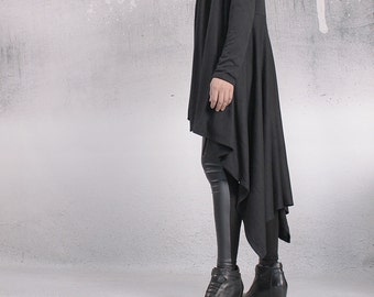 May include: A long black cardigan with a draped asymmetrical hemline. The cardigan is made of a soft, lightweight fabric and has long sleeves. The model is wearing the cardigan with black leggings and black wedge boots.