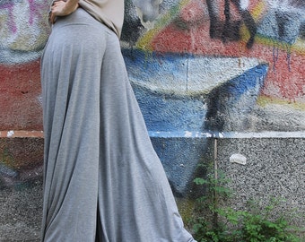 Può includere: Una donna indossa un paio di pantaloni grigi fluidi con una vestibilità ampia. I pantaloni sono realizzati in un tessuto morbido e drappeggiato e hanno una gamba larga.