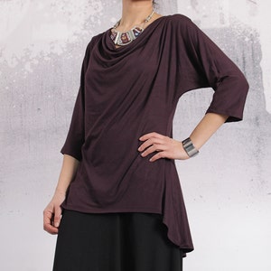 Puede incluir: Una blusa de manga larga, de color morado oscuro, con cuello de pico y escote drapeado. La blusa est&aacute; hecha de una tela suave y fluida y tiene un dobladillo ligeramente asim&eacute;trico.