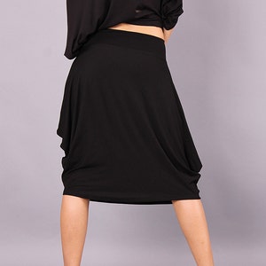 May include: A black midi skirt with a gathered design. The skirt is made of a soft, stretchy fabric and falls to the knee.