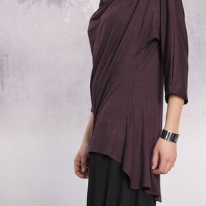 Puede incluir: Una blusa de manga larga, de color morado oscuro, drapeada con cuello de pico y un dobladillo alto-bajo. La blusa est&aacute; hecha de una tela suave y fluida.