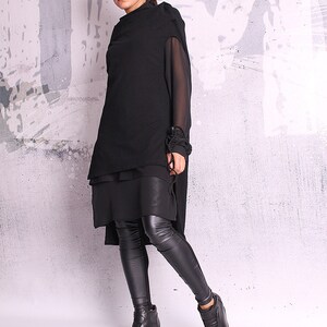 May include: A black layered tunic with long sleeves and a high neckline. The tunic is paired with black leggings and black wedge heeled ankle boots.
