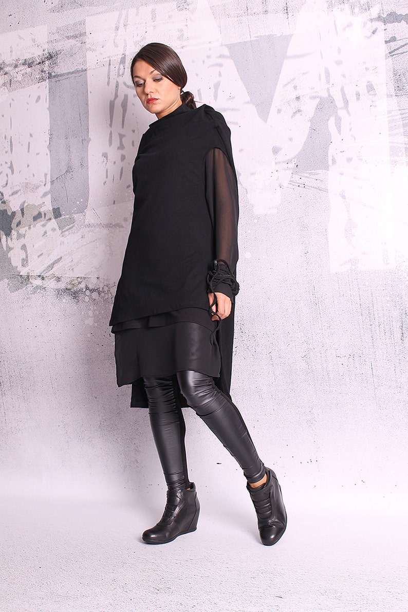 May include: A black layered tunic with long sleeves and a high neckline. The tunic is paired with black leggings and black wedge heeled ankle boots.