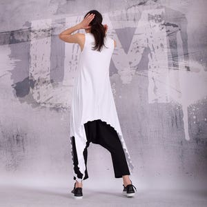 Op de afbeelding: Een witte, mouwloze tuniek met een hoge, lage zoom en een zwarte broek. De tuniek heeft een gerimpelde zoom en de broek is losjes gesneden.