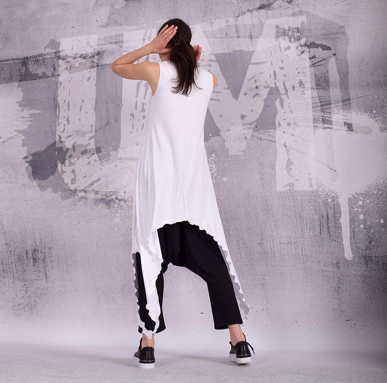 Op de afbeelding: Een witte, mouwloze tuniek met een hoge, lage zoom en een zwarte broek. De tuniek heeft een gerimpelde zoom en de broek is losjes gesneden.