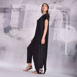 Puede incluir: Un vestido negro asim&eacute;trico de manga larga, con cuello redondo y falda amplia. El vestido est&aacute; hecho de una tela suave y c&oacute;moda y tiene un corte holgado.