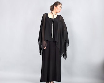 May include: A black sheer top with a long black skirt. The top has a long, thin silver necklace with a tassel.