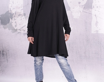 May include: A black off-the-shoulder tunic dress with long sleeves and a flowing hemline. The dress is paired with blue jeans and black ankle boots.