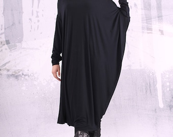 May include: A black long-sleeved dress with a loose, flowing fit. The dress has a scoop neckline and a slightly gathered hem. The model is wearing black boots.