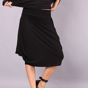 May include: A black midi skirt with a draped design. The skirt is made of a soft, stretchy fabric and falls to the knee.
