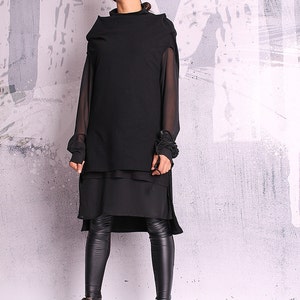 May include: A black layered tunic with sheer sleeves and a high neckline. The tunic is paired with black leggings and black ankle boots.
