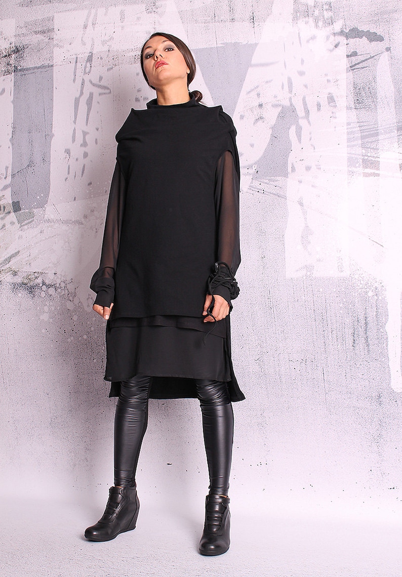 May include: A black layered tunic with sheer sleeves and a high neckline. The tunic is paired with black leggings and black ankle boots.