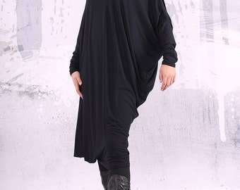 May include: A black long-sleeved tunic dress with a loose, flowing fit. The dress has a scoop neckline and long sleeves that are gathered at the wrists. The model is wearing the dress with black leggings and brown boots.