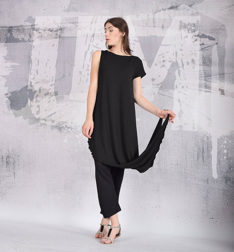 Puede incluir: Un vestido negro de manga larga con un dobladillo asim&eacute;trico drapeado. El vestido est&aacute; hecho de una tela suave y fluida y tiene un ajuste holgado. La modelo lleva el vestido con pantalones negros y sandalias.