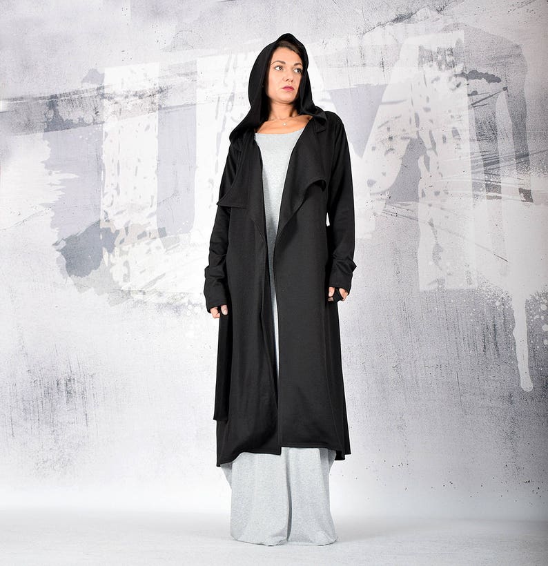 May include: A long black hooded cardigan with a draped front and long sleeves. The cardigan is made of a soft, lightweight fabric and has a relaxed fit.