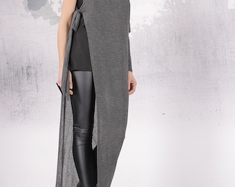 May include: A long, gray, one-shoulder tunic with a long sleeve and a tie detail at the shoulder. The tunic is worn with black leggings and black sandals.